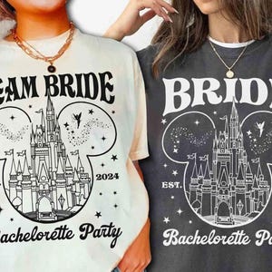 Può includere: Due magliette, una color crema e una antracite, con una grafica in bianco e nero. La grafica include un castello, stelle e le parole "TEAM BRIDE" e "BRIDE" sopra "Bachelorette Party" e l'anno "2024".