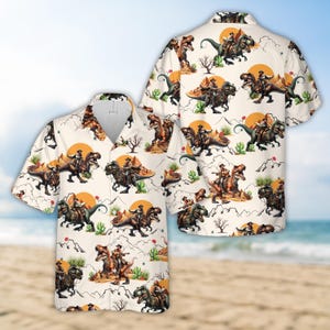 May include: A white short-sleeved button-down shirt with a repeating pattern of cowboys riding dinosaurs. The dinosaurs are brown and green and the cowboys are wearing brown hats and vests. The background is white with a yellow sun and green cacti.