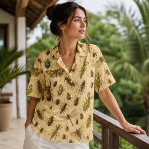 May include: A short-sleeved button-down shirt in a light yellow hue, featuring an all-over print of various insects including beetles, dragonflies, and moths in shades of brown, green, and black, with a classic collar and white buttons.