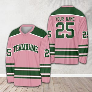 Pu&ograve; includere: Maglia da hockey rosa e verde con strisce bianche. La maglia ha il numero 25 sul davanti e il testo "YOUR NAME" sopra. Il retro della maglia ha il testo "TEAMNAME" e il numero 25 sulle maniche.