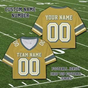 Puede incluir: Camiseta de f&uacute;tbol corta de color amarillo mostaza con detalles en blanco y azul marino. La camiseta presenta el texto "TEAM NAME" y "YOUR NAME" con el n&uacute;mero "00". La imagen tambi&eacute;n incluye el texto "CUSTOM NAME NUMBER" y "FOOTBALL JERSEY CROP TOP FOOTBALL JERSEY".