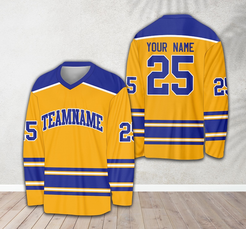 Pu&ograve; includere: Una maglia da hockey dorata con strisce blu e bianche. La maglia ha il testo "TEAMNAME" sul davanti e il numero "25" sul retro. Il testo "YOUR NAME" &egrave; sopra il numero.
