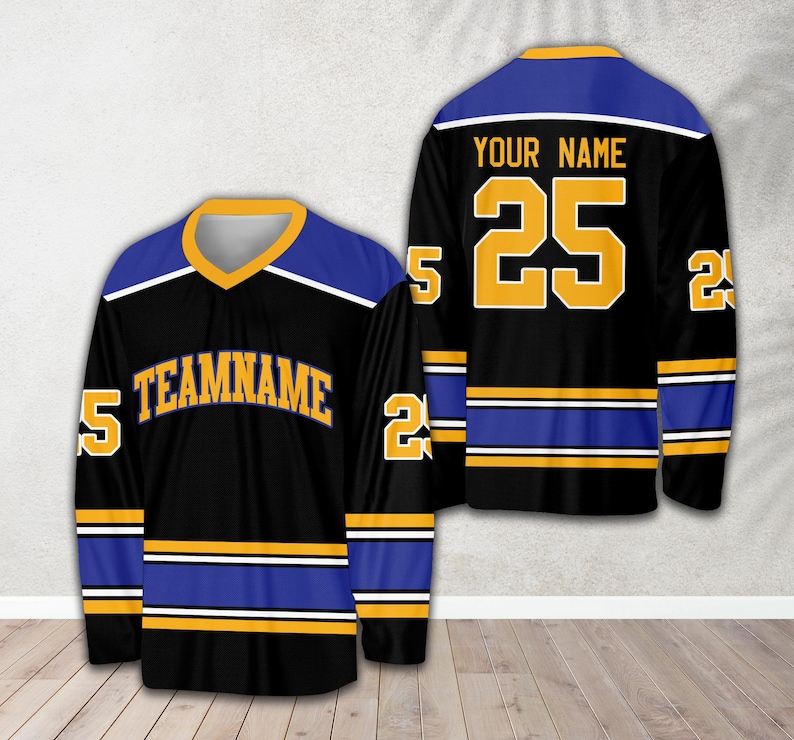 Pu&ograve; includere: Maglia da hockey nera con strisce blu e dorate. La maglia ha il testo "TEAMNAME" sul davanti e il numero "25" sul retro con il testo "YOUR NAME" sopra.