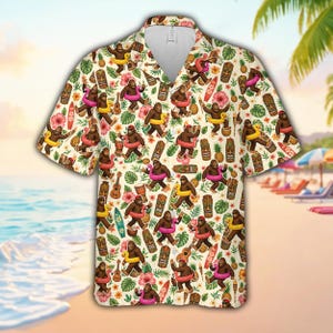 May include: A short-sleeve button-down shirt with a cream background featuring a repeating pattern of brown bigfoot creatures wearing colorful swim rings, interspersed with tiki masks, ukuleles, pineapples, surfboards, and pink hibiscus flowers.