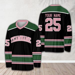 Pu&ograve; includere: Maglia da hockey nera con strisce verdi e rosa. La maglia ha il testo "TEAMNAME" in rosa e il numero "25" in rosa sul davanti. Il retro della maglia ha il testo "YOUR NAME" in rosa e il numero "25" in rosa.