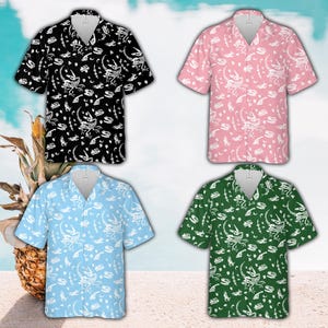 Puede incluir: Cuatro camisas de manga corta en negro, rosa, azul claro y verde. Cada camisa presenta un patrón de esqueleto de dinosaurio blanco. Una piña está en el fondo, lo que sugiere un tema tropical.