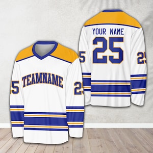 Pu&ograve; includere: Una maglia da hockey bianca con strisce blu e dorate. La maglia ha un collo a V e il numero 25 sul retro con il testo "YOUR NAME". La parte anteriore della maglia ha il testo "TEAMNAME" e il numero 25 sulle maniche.
