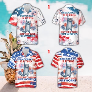 May include: Four short-sleeved shirts with a button-down collar, featuring a raccoon wearing sunglasses, fireworks, and the phrases "DEMOCRACY IS DYING" and "BUT HEY NICE FIREWORKS" in red, white, and blue.