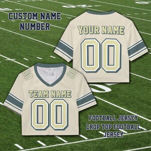 Puede incluir: Dos camisetas de f&uacute;tbol cortas color crema con detalles en verde azulado y dorado. Una camiseta muestra "TEAM NAME" y "00", la otra "YOUR NAME" y "00". El texto incluye "CUSTOM NAME NUMBER" y "FOOTBALL JERSEY CROP TOP FOOTBALL JERSEY".