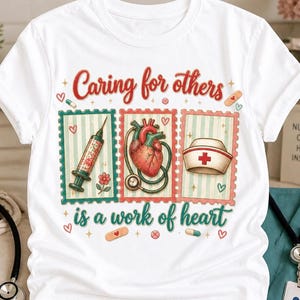 以下が含まれることがあります： Caring for others is a work of heartというテキストがプリントされた白いTシャツ。注射器、聴診器付きの解剖学的な心臓、ナースキャップが描かれた3つの長方形のフレームが配置され、小さなハートや錠剤のイラストが周囲に散りばめられています。