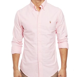 Pode incluir: Uma camisa rosa claro com botões e mangas compridas. A camisa tem gola abotoada e um pequeno logotipo bordado no peito. A camisa é feita de um tecido texturizado e tem um corte clássico.