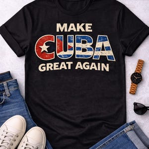 Puede incluir: Camiseta negra con el texto "MAKE CUBA GREAT AGAIN" en un estilo vintage. La palabra "CUBA" presenta los colores de la bandera cubana. La camiseta se muestra con vaqueros azules, zapatillas blancas, un reloj de madera y gafas de sol.