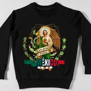 May include: Black sweatshirt featuring a graphic of San Judas Tadeo, a religious figure, with a halo, wings, and a staff. The design includes the text "SAN JUDAS TADEO" and "MEXICO" with the colors of the Mexican flag.