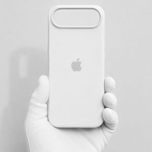 Pode incluir: Uma capa de smartphone branca sólida com um acabamento mate suave e um logótipo da Apple proeminente e centrado. A capa inclui um recorte horizontal alongado e distinto na parte superior, concebido para o módulo da câmara.