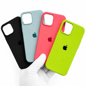 May include: Four silicone smartphone cases in black, light blue, coral, and lime green. Each case features a square camera cutout at the top left and a centered Apple logo. The cases are arranged in a fan shape, showcasing their smooth, matte finish.