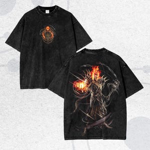 Könnte beinhalten: Zwei schwarze T-Shirts mit Used-Look. Eines zeigt ein feuriges Emblem auf der Vorderseite, das andere eine detaillierte Illustration eines Kriegers mit Flammen und einer Waffe auf dem Rücken. Beide haben kurze Ärmel und einen Rundhalsausschnitt.