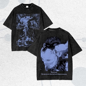 以下が含まれることがあります： 青いグラフィックデザインの黒いTシャツ2枚。1枚は「THE GHOST IN THE SHELL」のテキストが入った詳細なイラストが特徴です。もう1枚はロボットの顔と「Who are you? Who slips into my robot body and whispers to my ghost.」のテキストが表示されています。