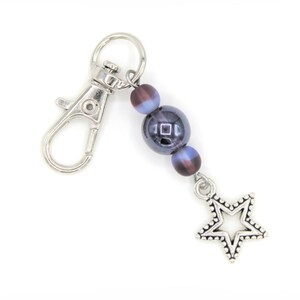 May include: A silver key chain with a star charm and two dark blue and purple beads.