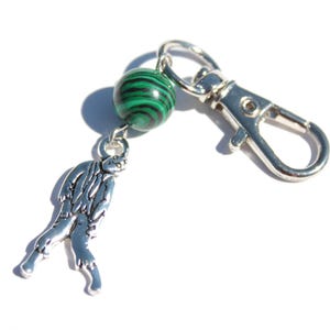 May include: A silver-toned keychain with a malachite green and black bead and a charm shaped like a mythical creature. The keychain has a silver clasp for easy attachment.