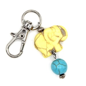 May include: A keychain with a yellow elephant charm and a turquoise bead. The elephant charm is intricately carved and hangs from a silver-coloured clasp. The turquoise bead provides a vibrant contrast.