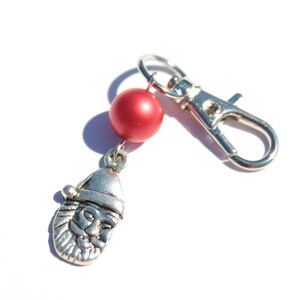 May include: A silver-coloured keychain featuring a Santa Claus charm and a red bead. The charm depicts Santa's face and hat. The keychain has a silver clasp for attaching to keys or bags.