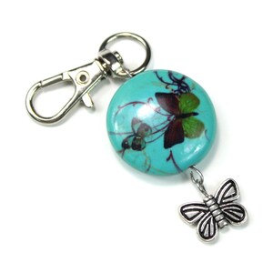 May include: A turquoise blue key chain with a silver metal lobster clasp and a silver metal butterfly charm. The turquoise blue bead features a printed design of butterflies.