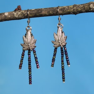 Könnte beinhalten: Ein Paar silberne Ohrringe mit einem Marihuana-Blatt-Anhänger und schimmernden schwarzen Perlen.