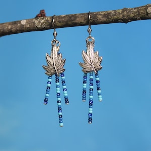May include: Silver dangle earrings with a marijuana leaf charm and blue and turquoise beads.