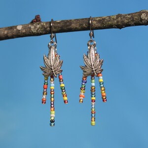 May include: Silver dangle earrings with a marijuana leaf charm and colourful beads hanging from the bottom.