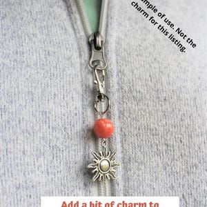 May include: A silver zipper pull charm with a coral-colored bead and a sunburst pendant. The text "Add a bit of charm to your jacket!" is displayed at the bottom of the image.