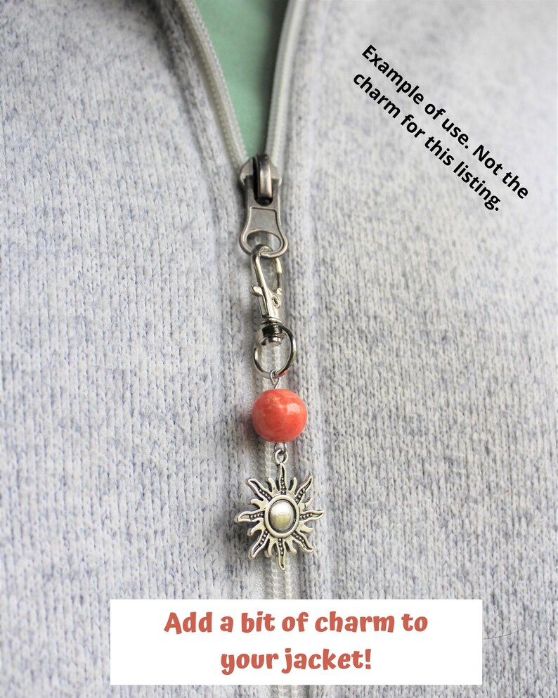 May include: A silver zipper pull charm with a coral-colored bead and a sunburst pendant. The text "Add a bit of charm to your jacket!" is displayed at the bottom of the image.
