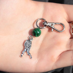 May include: A silver-toned keychain with a lobster clasp, a green and black marbled bead, and a small, detailed zombie charm. The keychain is designed to attach to keys or bags.