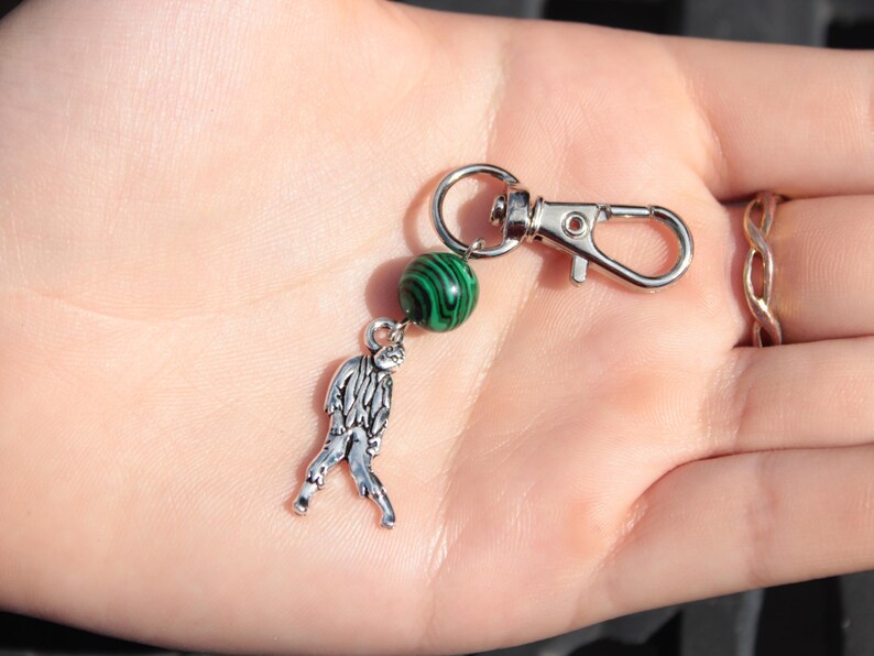 May include: A silver-toned keychain with a lobster clasp, a green and black marbled bead, and a small, detailed zombie charm. The keychain is designed to attach to keys or bags.