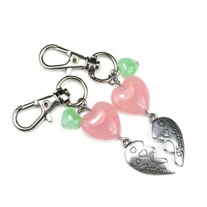 May include: Two keyrings with silver clasps. Each keyring has a pink heart-shaped bead, a green heart-shaped bead, and a silver charm. One charm says "Mother" and the other says "Daughter".