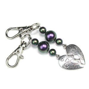 May include: Two silver keyrings with lobster claw clasps. Each keyring has a strand of dark purple and green iridescent beads. The strands connect to two halves of a heart pendant, one half reading "Mother" and the other "Daughter".