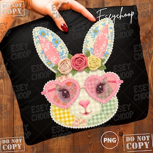 Peut inclure: Coussin décoratif noir avec un visage de lapin fantaisiste orné de lunettes de soleil en forme de cœur et d'éléments floraux. Le lapin a des détails en patchwork et une couronne de fleurs. Le coussin est tenu par une main.
