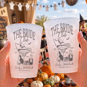 May include: Two frosted plastic cups featuring black printed text that reads THE BRIDE Club, EST. 2026, and Emily's Witcholorette NEW ORLEANS, LA. The design includes illustrations of a witch hat, a cocktail glass, a broom, and a skull.