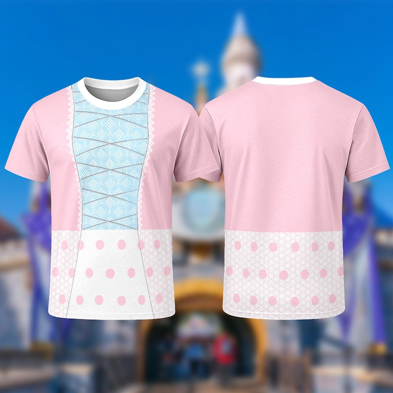 Puede incluir: Camiseta rosa con un dise&ntilde;o que simula un vestido. La parte delantera tiene un detalle de cors&eacute; azul claro con ribete de encaje blanco y un estampado de lunares blancos. La parte trasera es rosa liso con un estampado de lunares blancos en la parte inferior.