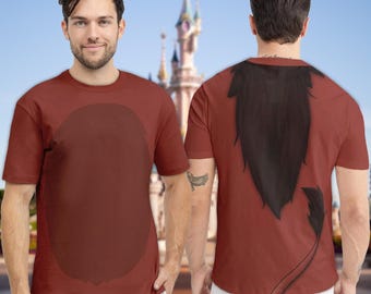 Pode incluir: Uma camiseta marrom com um design oval marrom na frente e um design de juba e cauda de leão preto nas costas. A camisa é de manga curta e parece ser feita de um material macio. O fundo apresenta um castelo.