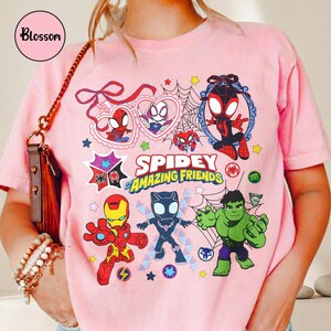 K&ouml;nnte beinhalten: Hellrosa T-Shirt mit dem Schriftzug "Spidey and Amazing Friends" und Cartoon-Illustrationen von Spider-Man, Iron Man, Hulk und Black Panther. Das Shirt hat einen Rundhalsausschnitt und kurze &Auml;rmel.