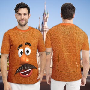 May include: Orange t-shirt featuring a cartoon Mr. Potato Head face on the front. The shirt has a textured appearance and an orange collar. The back of the shirt has a pocket-like design.