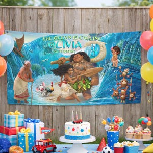 May include: A rectangular party banner featuring a Moana-themed graphic with a large ocean wave, characters including Moana, Maui, and Pua, and the text THE OCEAN IS CALLING OLIVIA IS TURNING 3. The banner is displayed against a wooden fence background.