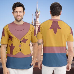 May include: A short-sleeved t-shirt featuring a cartoon design. The shirt has a yellow vest design over a pink shirt, with a blue bottom. The back of the shirt has a yellow background with a pink stripe and a large maroon design.