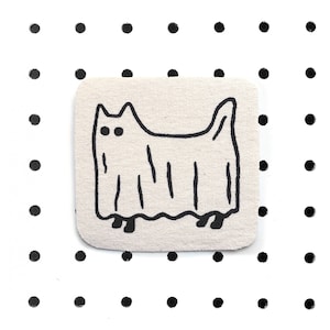 Könnte beinhalten: Ein weißer Stoff-Patch mit einer schwarzen Umrandung einer Katze, die als Geist verkleidet ist. Die Katze hat zwei schwarze Augen und steht auf zwei schwarzen Füßen.