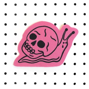 May include: A pink fabric patch with a black outline of a snail with a skull for a shell.