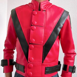 May include: A red jacket with black accents, featuring a stand-up collar and multiple large buttons down the front. The jacket has black stripes across the shoulders and a belt detail at the waist and cuffs. The jacket is made of a shiny material.
