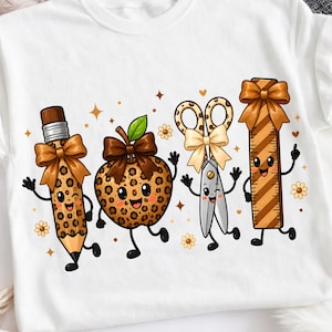 Puede incluir: Una camiseta blanca con un estampado gráfico de cuatro útiles escolares antropomórficos: un lápiz con estampado de leopardo, una manzana con estampado de leopardo, unas tijeras y una regla, decorados con lazos marrones y crema y flores.
