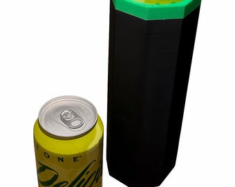 Puede incluir: Una lata de refresco amarilla y verde junto a un enfriador de latas negro y verde. La lata tiene las palabras "ONE" y "Delicious" impresas. El enfriador es hexagonal.