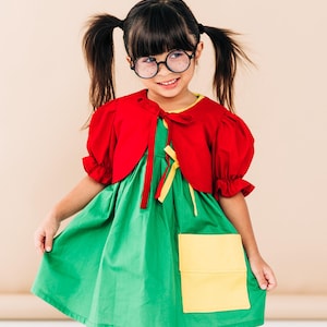 May include: A child's costume featuring a green dress with a yellow pocket, a red bolero jacket, and round glasses. The outfit includes white bloomers and is styled with pigtails. The costume has a playful and whimsical appearance.