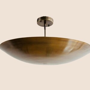 May include: A bronze-colored, bowl-shaped ceiling light fixture. The fixture has a circular base and a central rod connecting to a large, shallow bowl. The light is suspended from the ceiling.